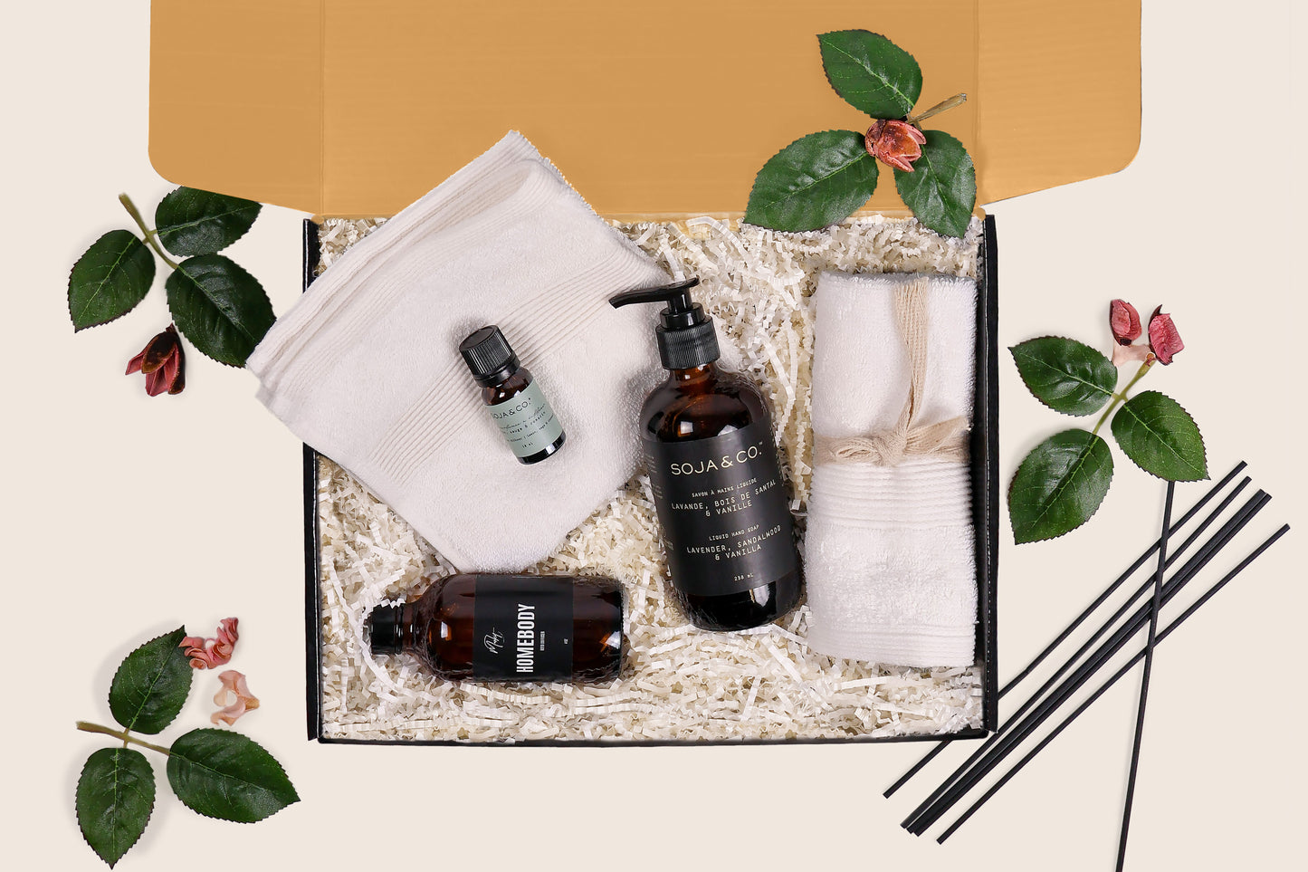 Serenity Luxe gift box with hand soap, essential oil, diffuser, and wash cloths arranged in crinkle paper, with greenery accents and kraft gift box.
