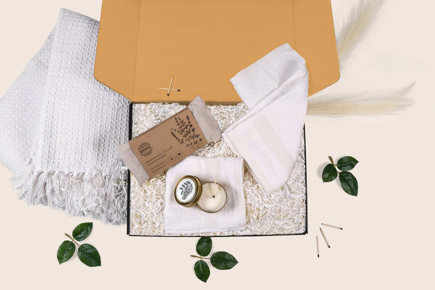 Unboxing of Relaxation Retreat gift set featuring a lavender eye pillow, woven throw, candle, and wash cloths in a kraft box with greenery.
