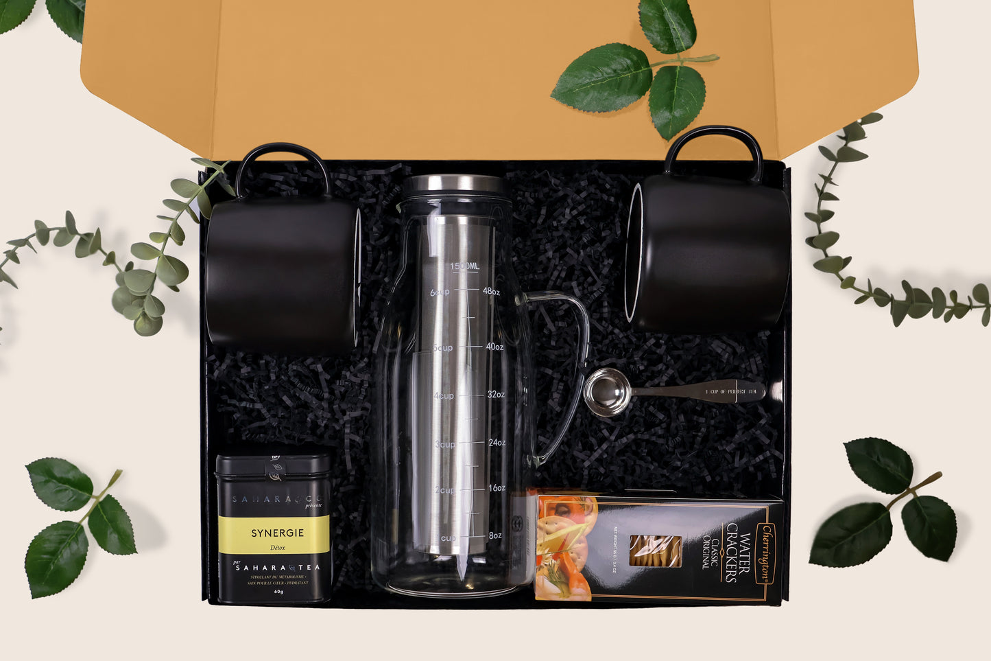 Sunday Tea Ritual gift box open to reveal black mugs, glass tea infuser, Synergy tea, crackers, and a teaspoon arranged in shredded paper.