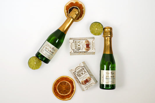 Flat lay of Bubbly & Sweet gift set with two bottles of Oddbird non-alcoholic sparkling wine, Cashew Roca chocolates, and dried citrus slices.