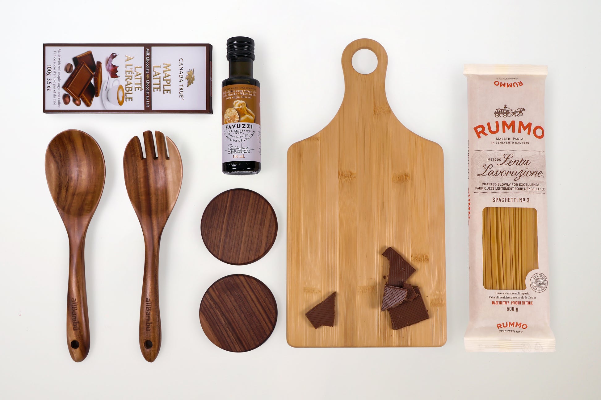 Flat lay of curated gourmet gift box items including truffle oil, Rummo spaghetti, maple chocolate, bamboo board, and wooden utensils