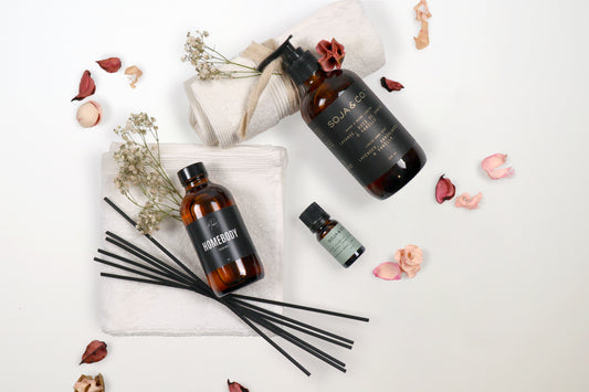 Flat lay of Serenity Luxe gift box items including reed diffuser, lavender hand soap, essential oil, and cotton wash cloths, surrounded by dried florals on a white background.